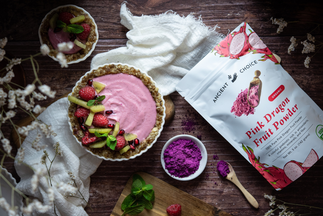 Raw pink dragon fruit tart and mini tart with fruit toppings, next to pouch and bowl of powder.