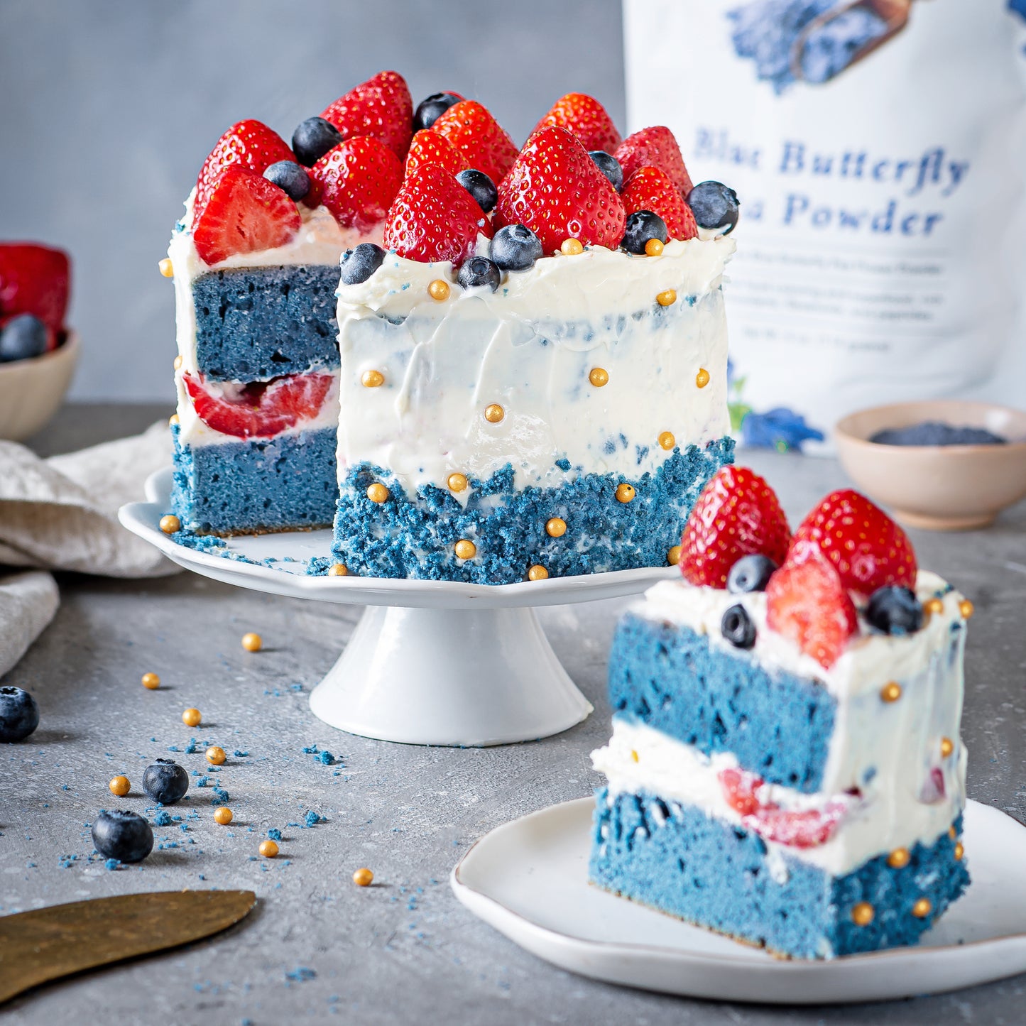 Blue layered cake made with Ancient Choice Butterfly Pea Powder and white frosting, topped with fresh berries.