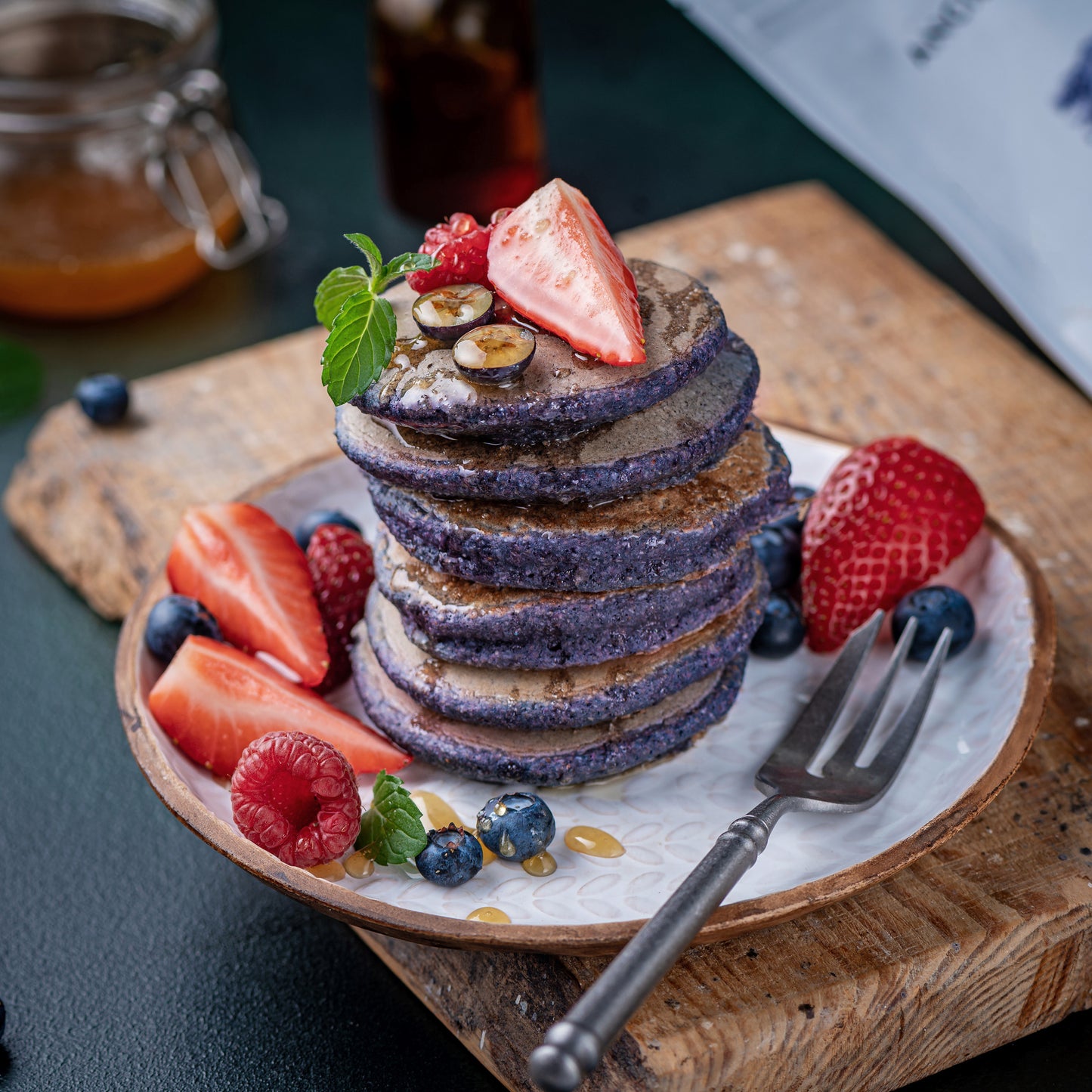 Blueberry pancakes made with Ancient Choice Wild Blueberry Powder, topped with fresh berries, mint, and honey drizzle on a white plate.