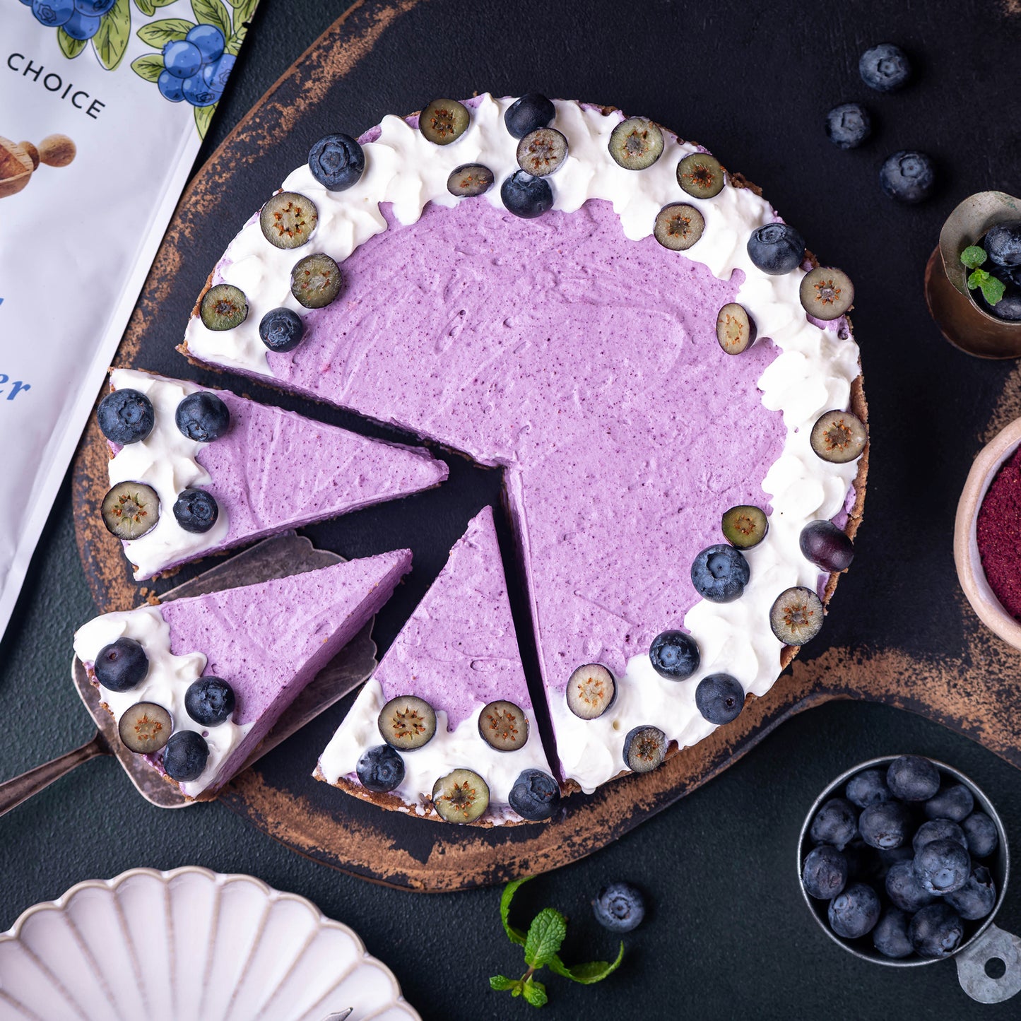 Blueberry cheesecake made with Ancient Choice Wild Blueberry Powder, topped with fresh blueberries and cream on a rustic serving board.