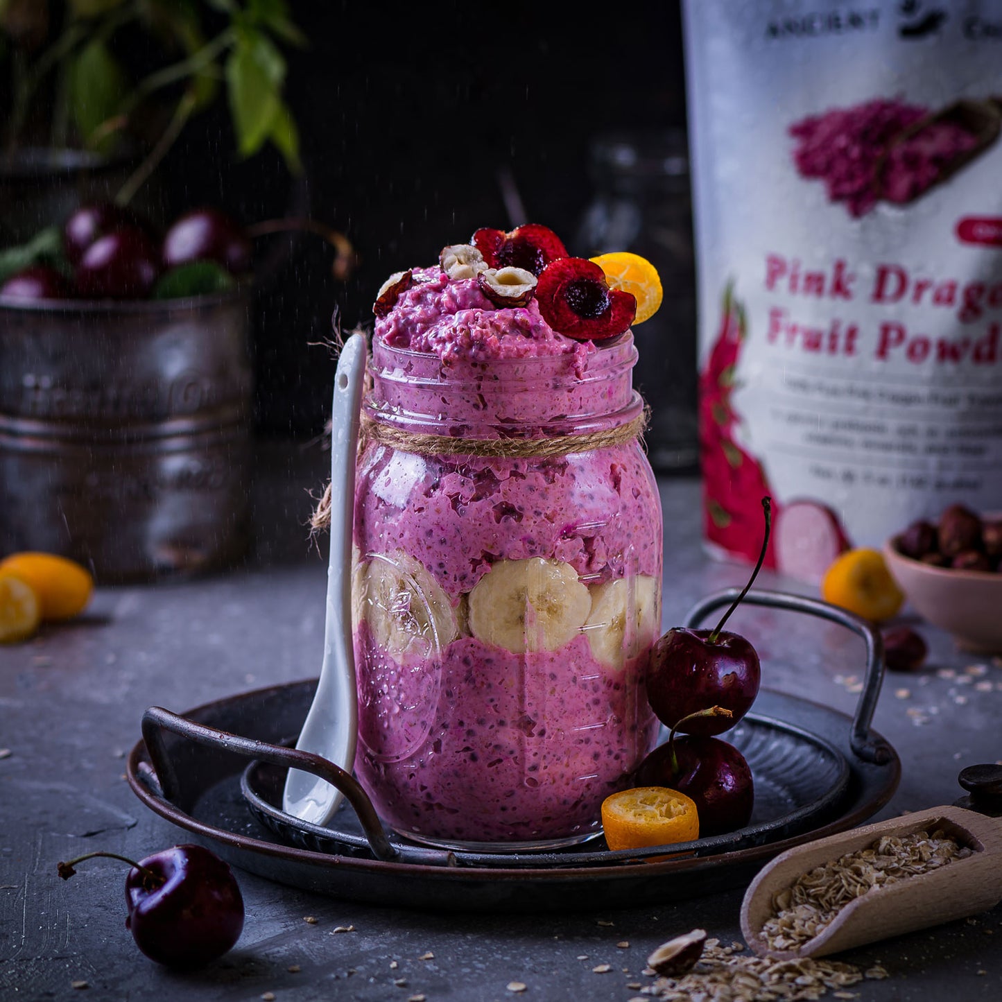 Overnight oats made with Ancient Choice Pink Dragon Fruit Powder, layered with banana slices and topped with cherries, hazelnuts, and kumquat.