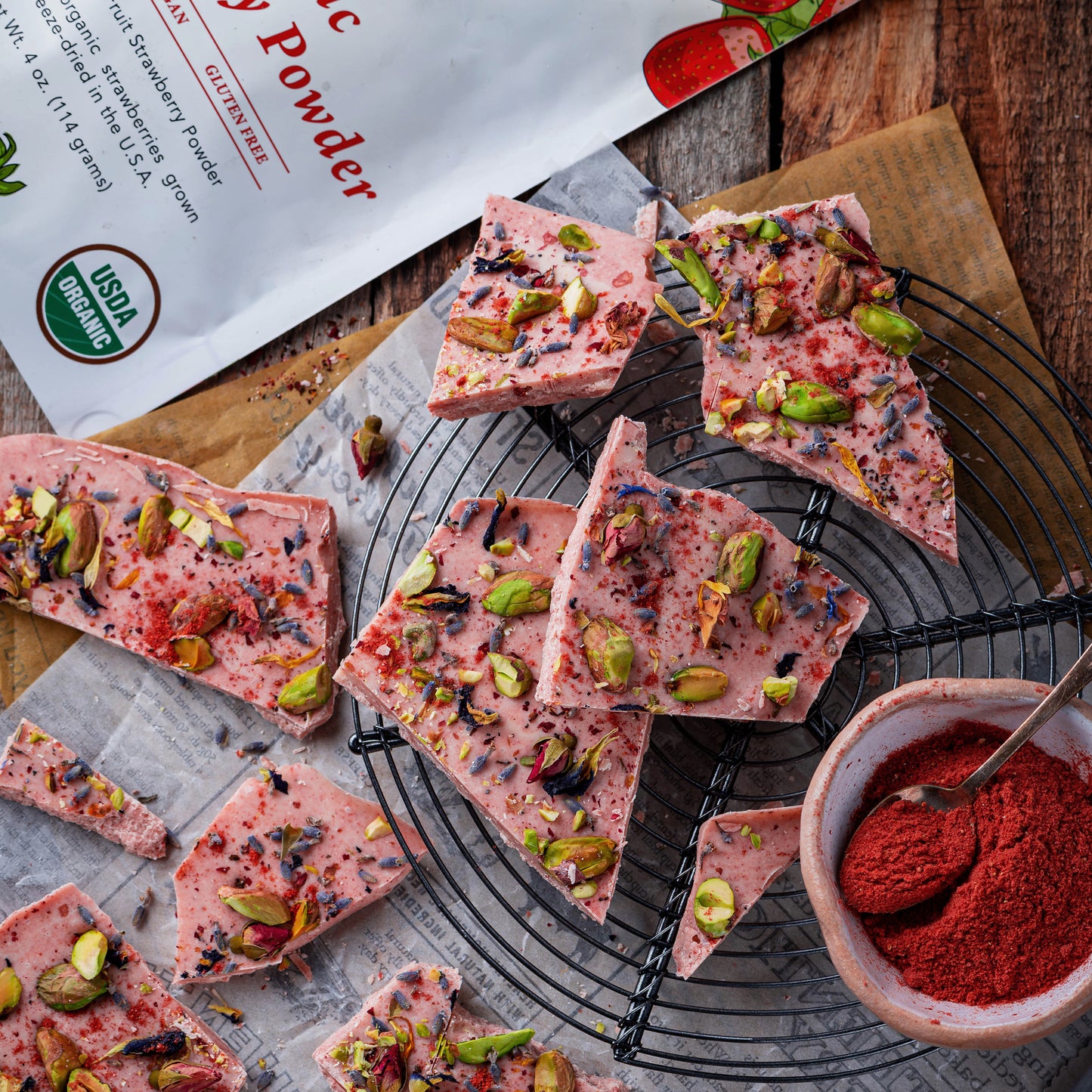 White chocolate bark made with Ancient Choice Strawberry Powder, topped with pistachios, and dried flowers on parchment paper.
