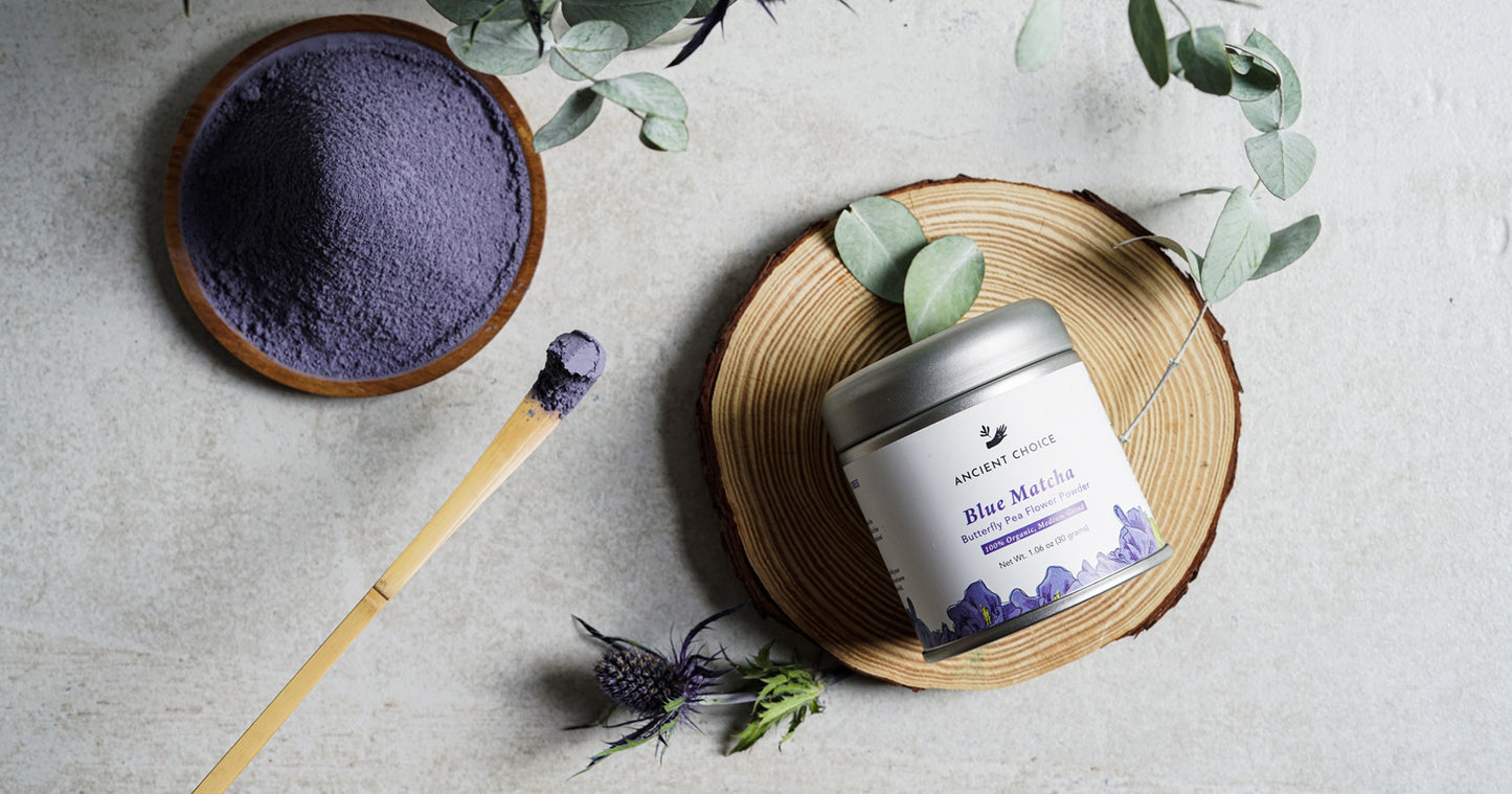 Ancient Choice Blue Matcha displayed in a wooden bowl and tin, with a bamboo spoon and botanical accents on a neutral background.