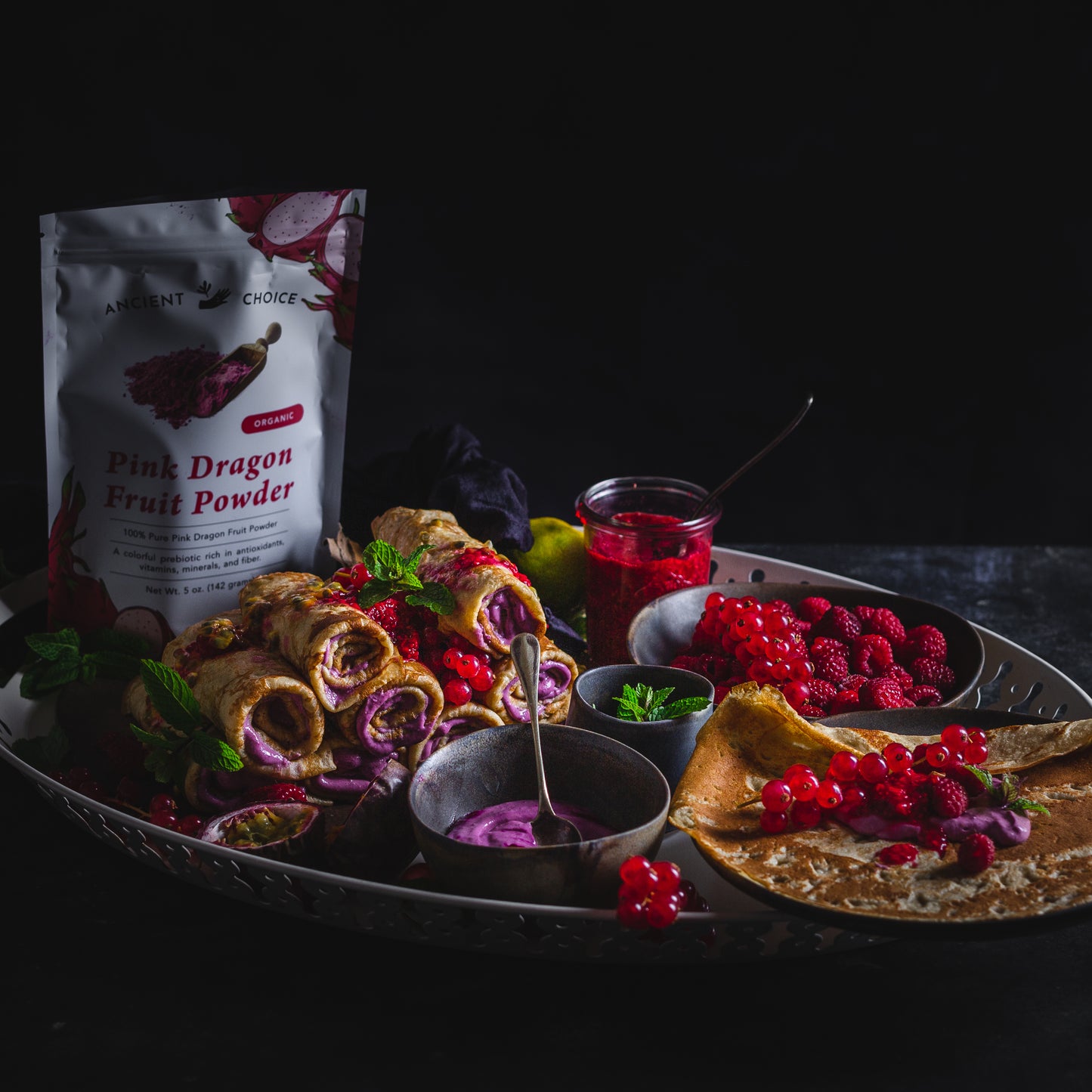 Crepes filled with a cream made with Ancient Choice Dragon Fruit Powder, served with fresh berries and pomegranate seeds on a silver tray.