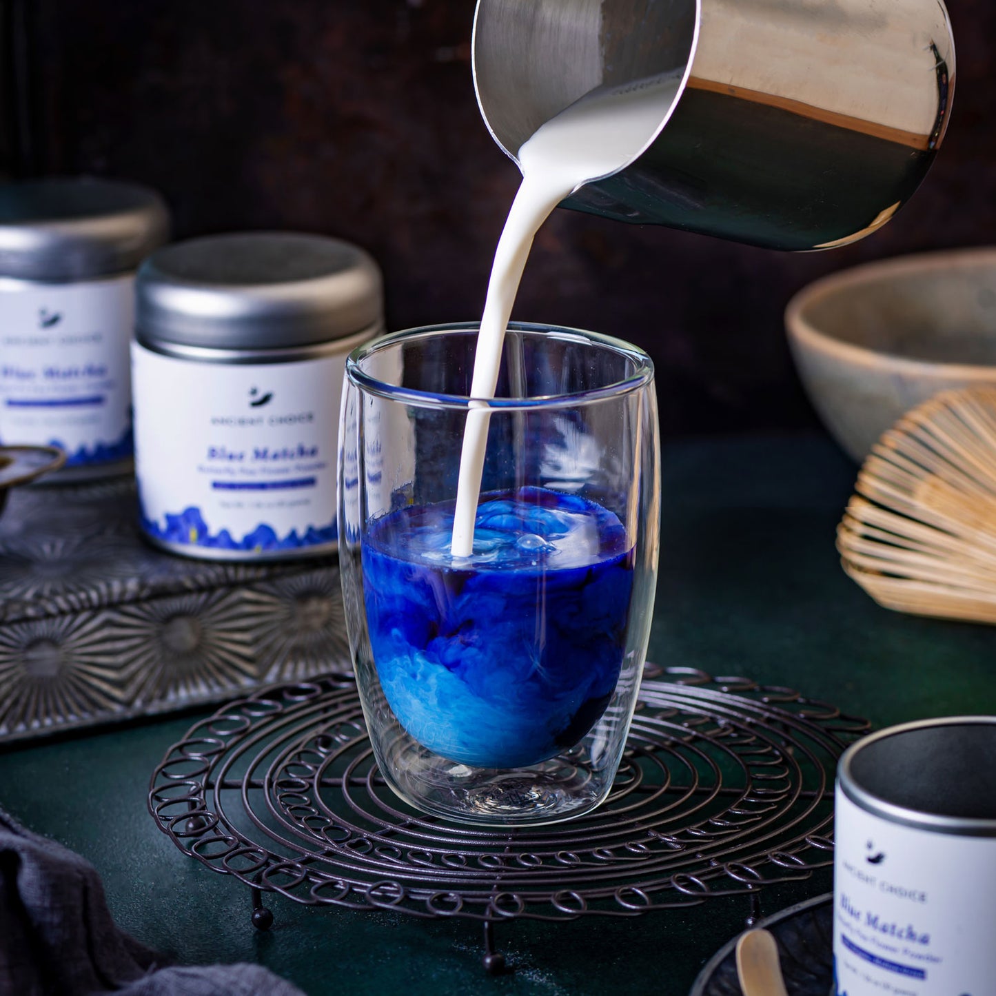 Milk being poured into a glass of Ancient Choice Blue Matcha