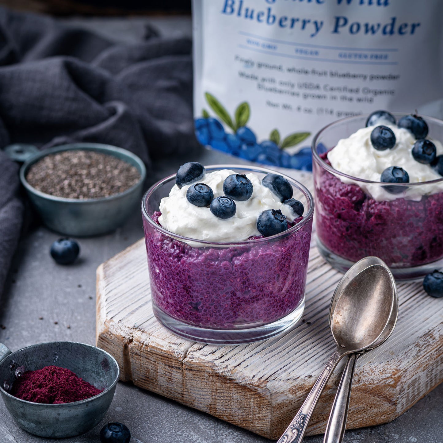 Blueberry chia pudding made with Ancient Choice Wild Blueberry Powder, topped with whipped cream and fresh blueberries on a wooden board.