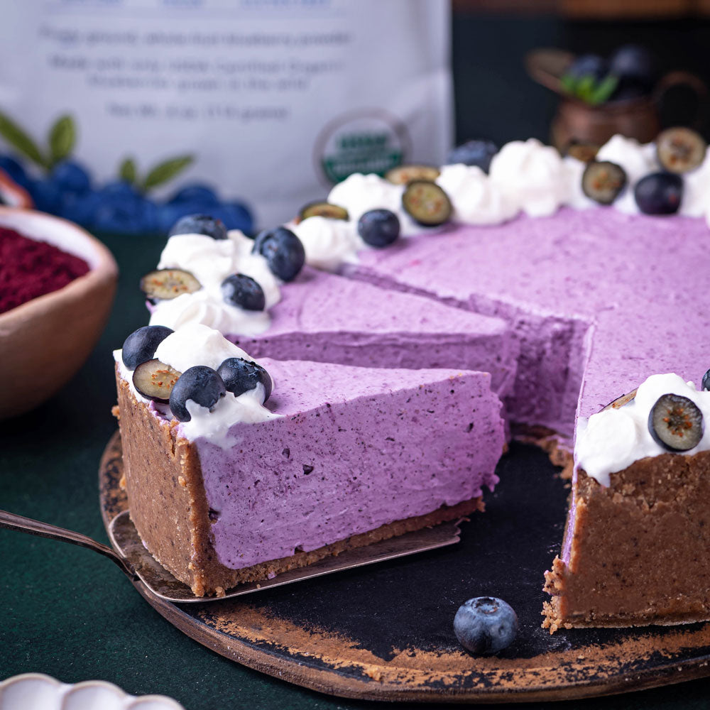 Blueberry cheesecake made with Ancient Choice Wild Blueberry Powder, topped with cream and berries on rustic plate.