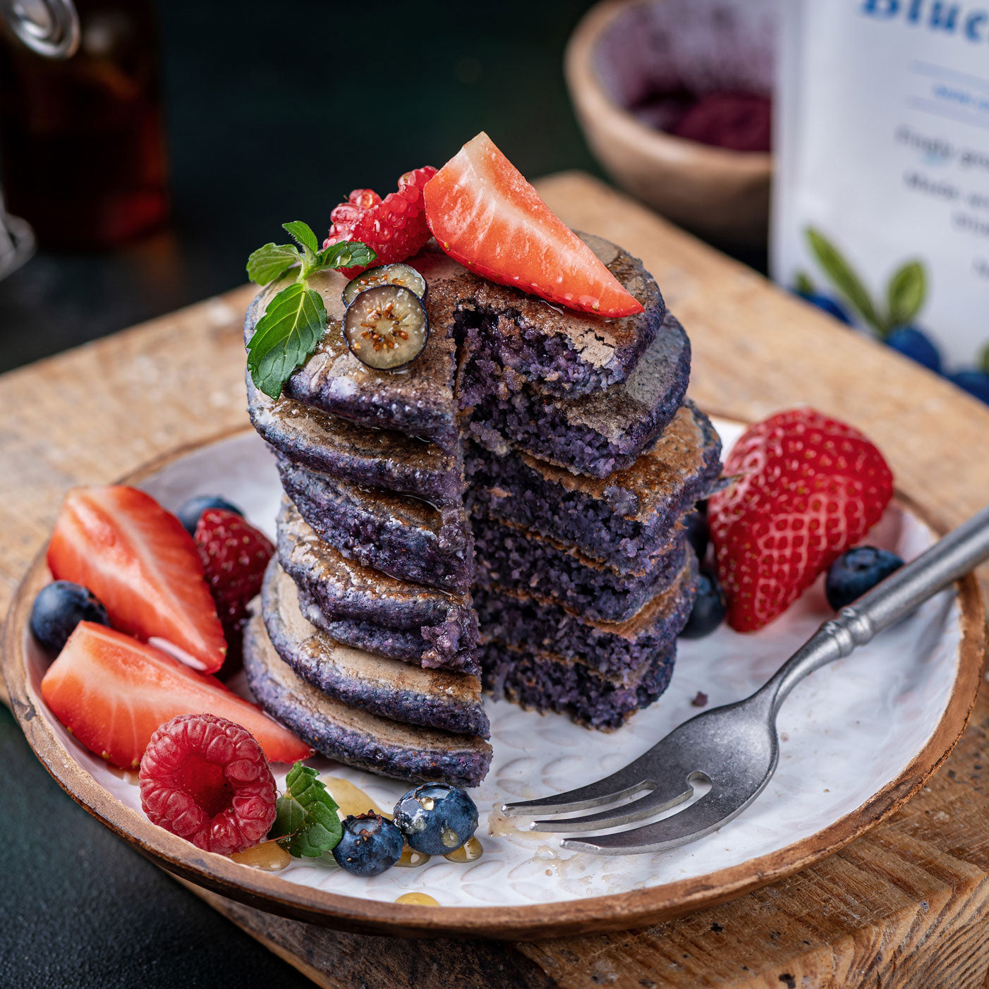 Blueberry pancakes made with Ancient Choice Wild Blueberry Powder, served with fresh berries and syrup on a ceramic plate.