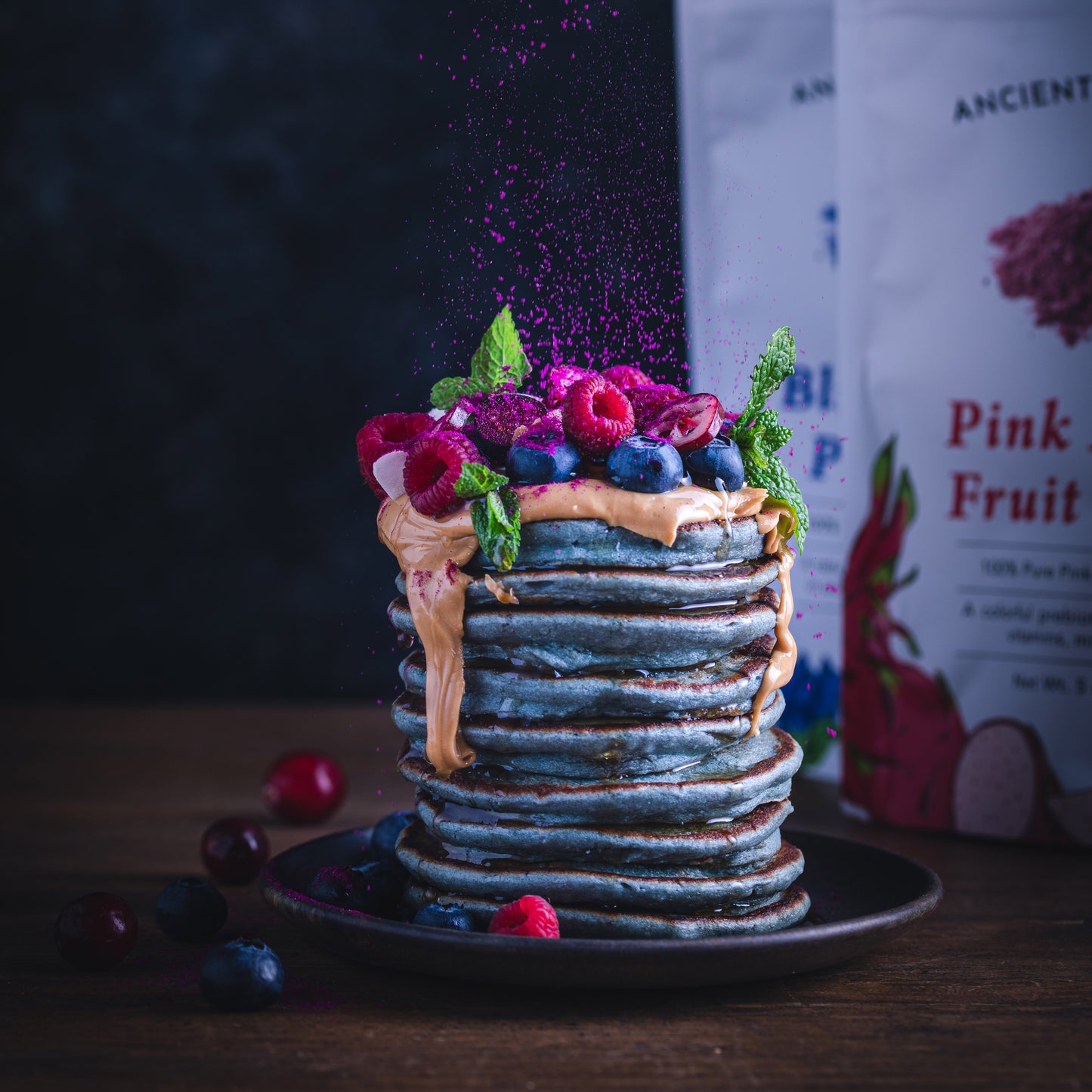 Stack of blue pancakes made with Ancient Choice Butterfly Pea Flower Powder, topped with peanut butter, fresh berries, and a sprinkle of Ancient Choice Dragon Fruit Powder.