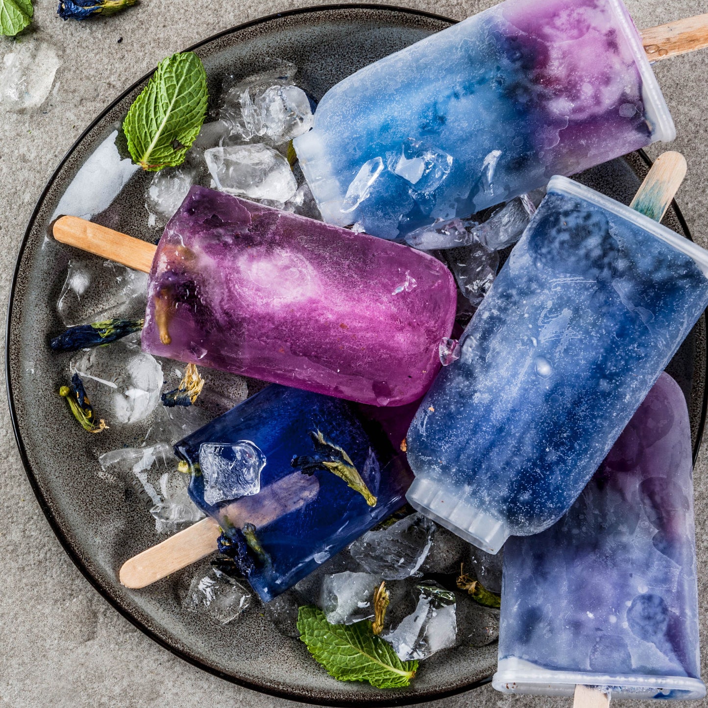Popsicles made with Ancient Choice Butterfly Pea Flower Powder, served in a bowl with ice cubes and mint leaves.