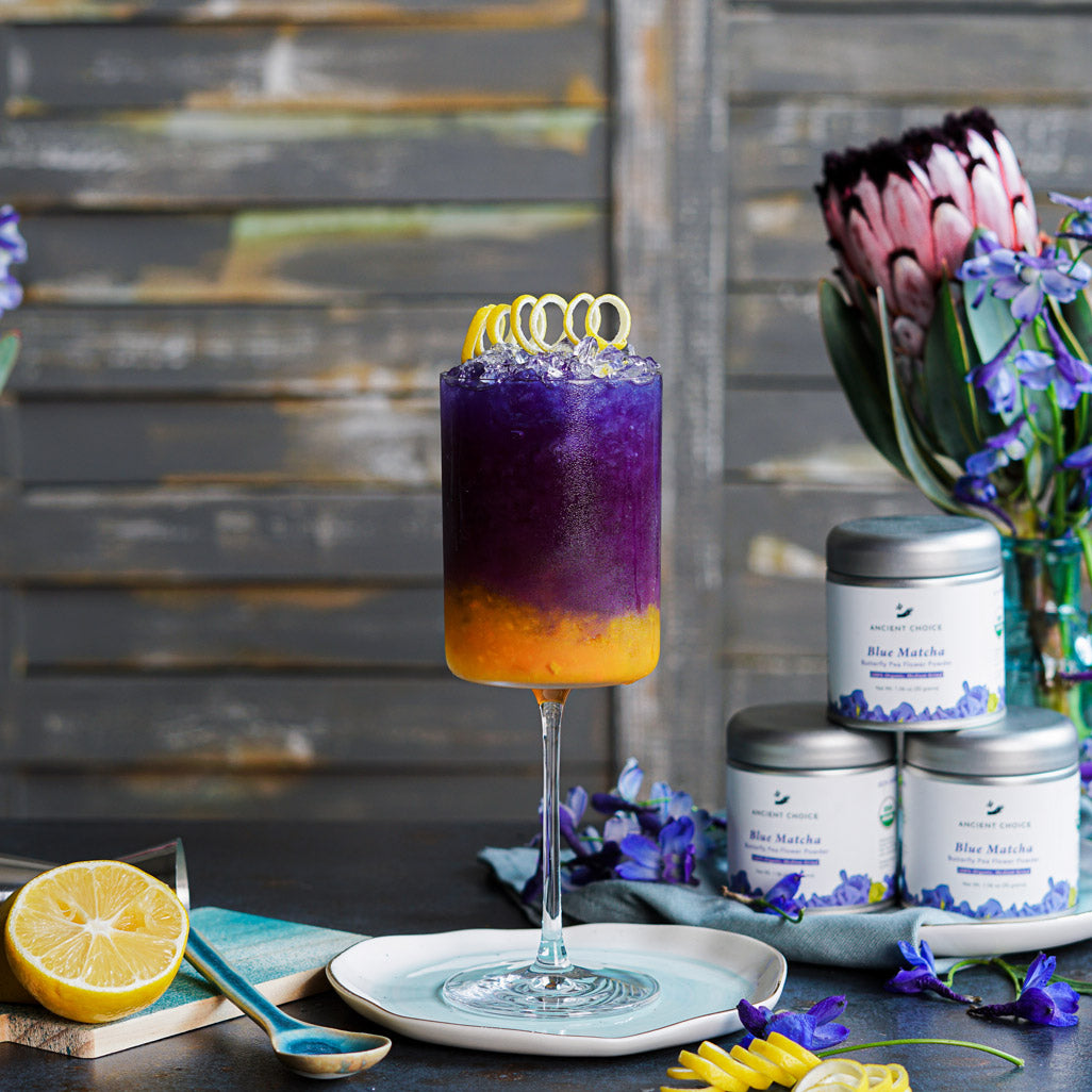 Layered drink made with Ancient Choice Blue Matcha, served in a glass and topped with lemon curls.