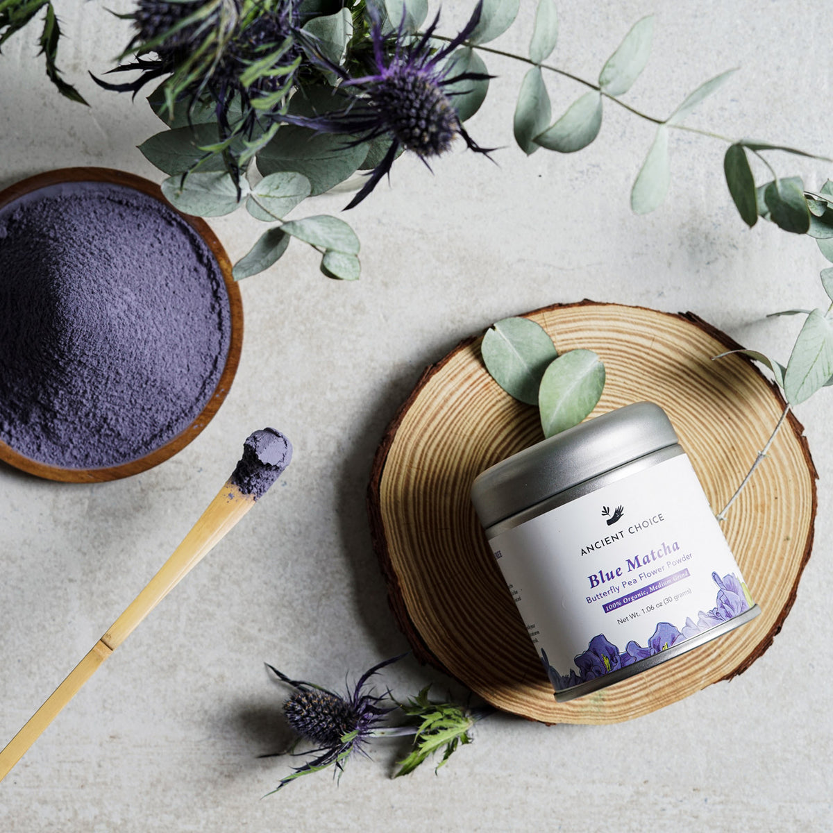 Ancient Choice Blue Matcha tin canister, shown with a wooden spoon and botanical decor.