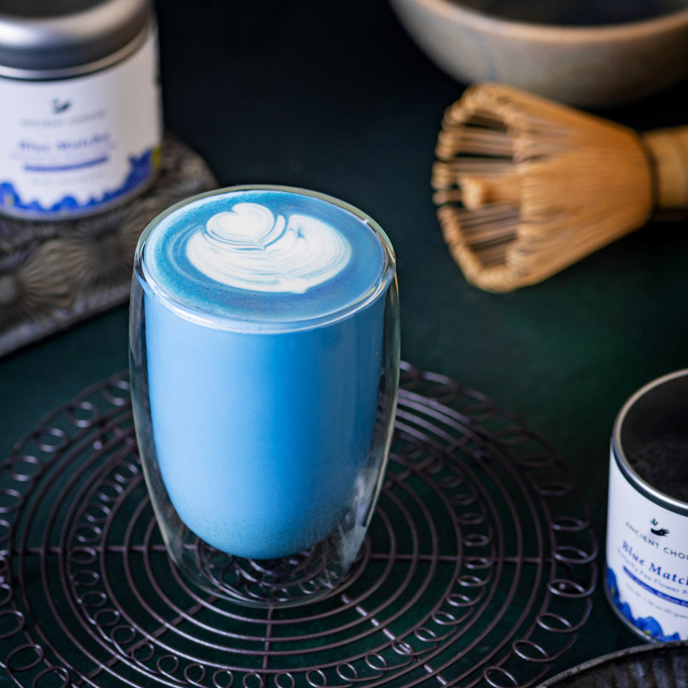 Ancient Choice Blue Matcha Latte served in a clear glass with heart-shaped foam art.